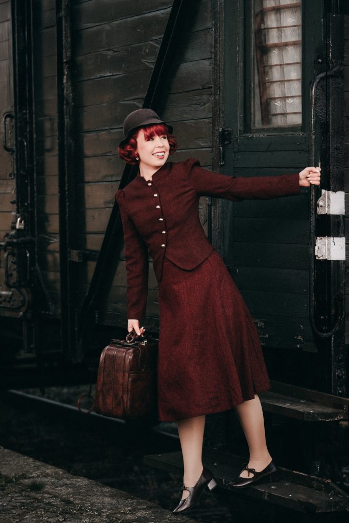 Frau in rotem Kleid mit Aktenkoffer auf einer Treppe, lächelnd und in modischer Pose.